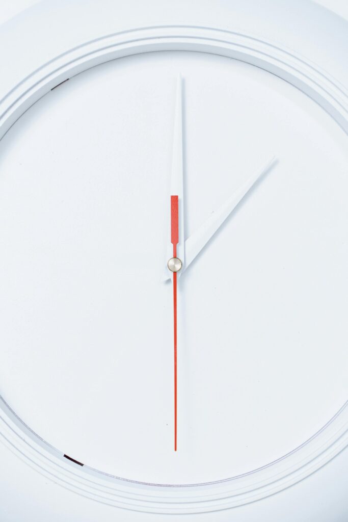 A close-up of a sleek white wall clock with minimalist design, featuring red and white clock hands.